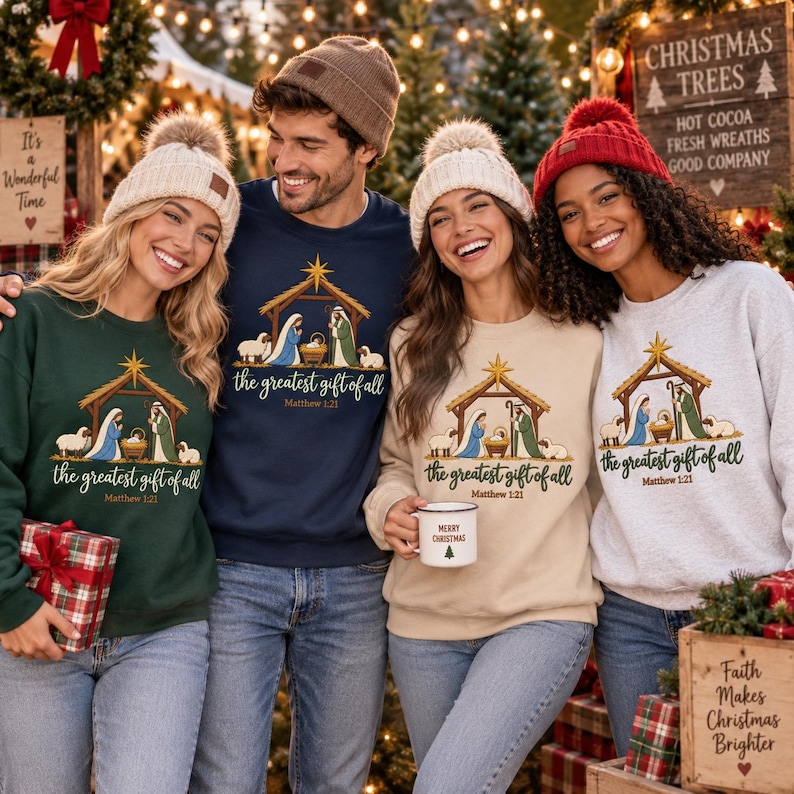 May include: Four people wearing matching crewneck sweatshirts featuring a nativity scene graphic with the text "the greatest gift of all Matthew 1:21". The sweatshirts are in dark green, navy blue, beige, and light gray, paired with knit beanies.