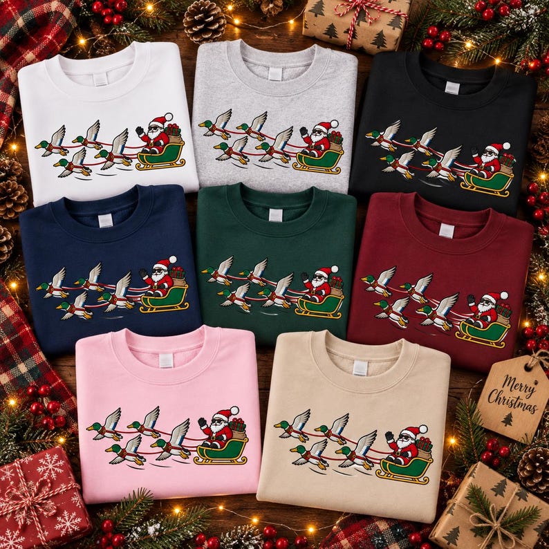 May include: A collection of eight crewneck sweatshirts in white, gray, black, navy, dark green, maroon, pink, and beige. Each sweatshirt features a graphic of Santa Claus in a green sleigh pulled by a team of flying mallard ducks in flight.