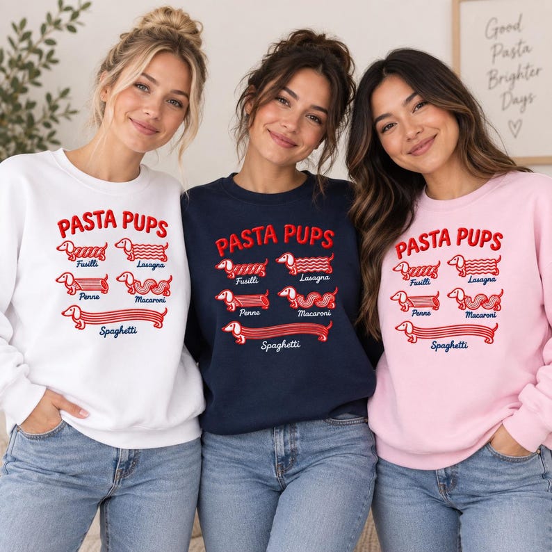 May include: Three crewneck sweatshirts in white, navy blue, and light pink. Each features red embroidered text reading PASTA PUPS above illustrations of dachshunds shaped like pasta types labeled Fusilli, Lasagna, Penne, Macaroni, and Spaghetti.