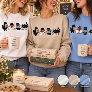 May include: Three crewneck sweatshirts in white, beige, and light blue, each featuring a graphic of four black cats reading books. The sweatshirts display text including Good Books Brighter Friends, Book Club, and Books People Happier Days.