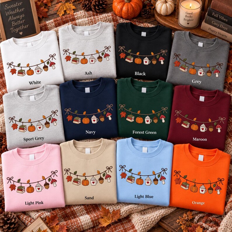 May include: A collection of twelve crewneck sweatshirts in various colors, including white, ash, black, grey, sport grey, navy, forest green, maroon, light pink, sand, light blue, and orange. Each features an embroidered garland of autumn items.