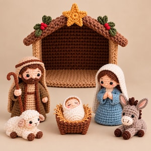 May include: A crochet nativity set featuring a stable with a yellow star, a figure in a brown robe with a staff, a figure in a blue dress with a white head covering, a swaddled infant in a manger, a white lamb, and a gray donkey.