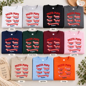 May include: A collection of eleven crewneck sweatshirts in various colors, each featuring the red text PASTA PUPS above illustrations of dachshunds shaped like pasta types including fusilli, lasagna, penne, macaroni, and spaghetti.