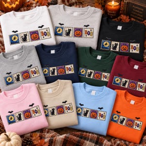 May include: A collection of crewneck sweatshirts in various colors, each featuring a horizontal row of four rectangular stamps. The stamps display a witch on a broom, a black cat, a jack-o'-lantern, and the text BOO, accented by small bats.
