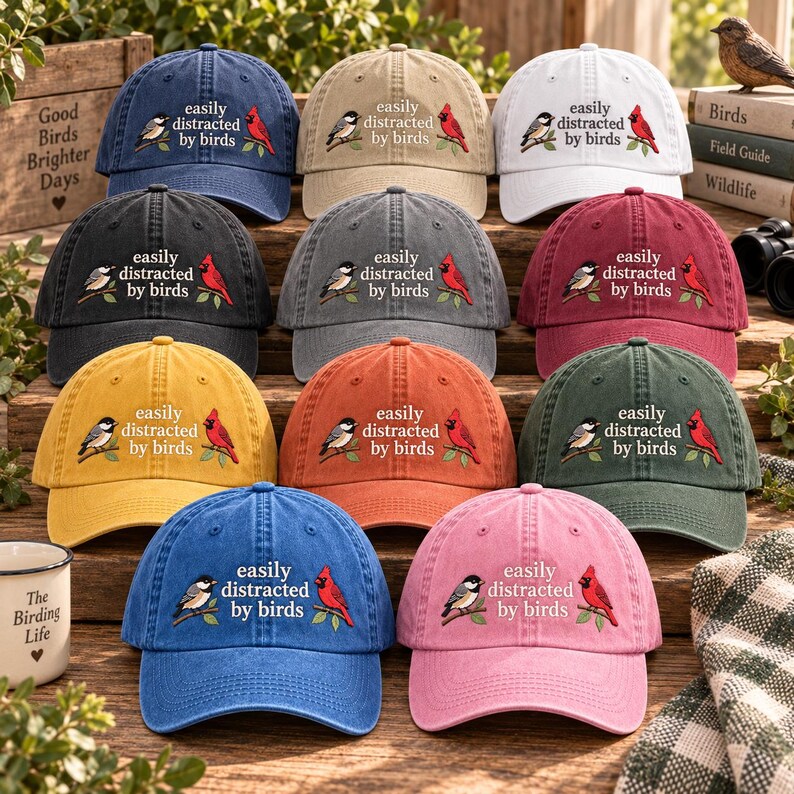 May include: A collection of eleven baseball caps in various colors, each featuring the embroidered text 'easily distracted by birds' alongside illustrations of a black-capped chickadee and a red cardinal perched on green branches.