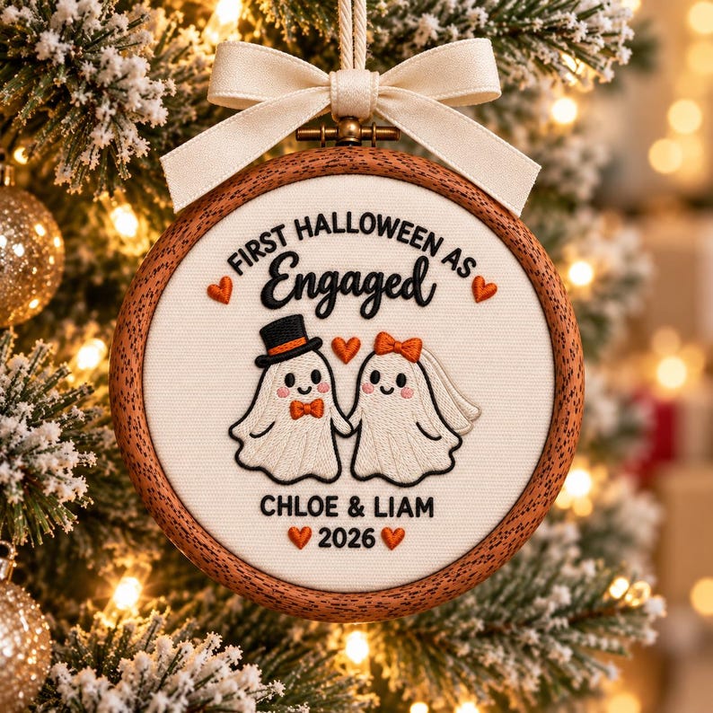 May include: A round wooden embroidery hoop ornament featuring white fabric with embroidered text First Halloween as Engaged, two ghost figures, and the names Chloe & Liam with the year 2026. A cream-colored ribbon bow is attached to the top.