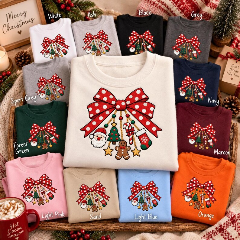 May include: A collection of crewneck sweatshirts in various colors, each featuring a central graphic of a large red and white polka dot bow with hanging Christmas ornaments including a Santa face, a tree, a candy cane, and a gingerbread man.