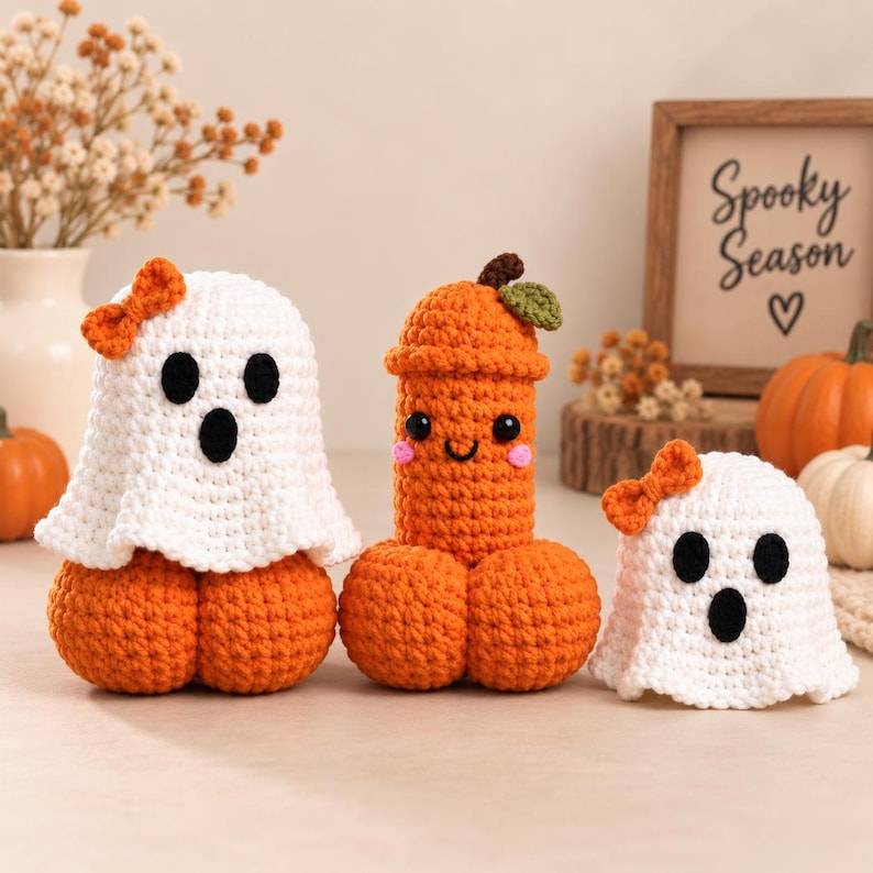 May include: Two crocheted white ghosts with orange bows and black eyes and mouths, and one central orange crocheted phallic figure with a small green leaf, black eyes, a smile, and pink cheeks. A framed sign reads Spooky Season with a heart.