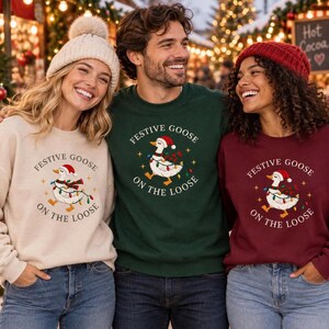 May include: Three crewneck sweatshirts featuring a graphic of a goose wearing a Santa hat and wrapped in colorful Christmas lights. The text "FESTIVE GOOSE ON THE LOOSE" is printed in a circular pattern around the goose illustration on each shirt.