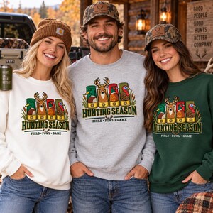 May include: Three crewneck sweatshirts in white, heather gray, and dark green, each featuring a graphic of four shotgun shells topped with a mallard, deer, pheasant, and turkey, with the text Hunting Season Field Fowl Game printed below.