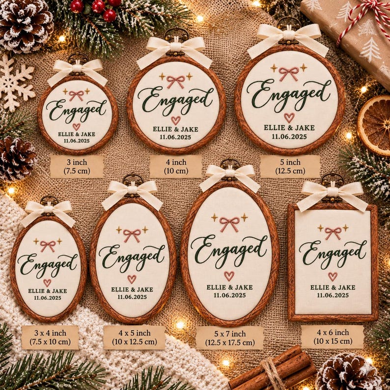 May include: A collection of wooden-framed embroidery hoops and a rectangular frame featuring white fabric with the embroidered text Engaged, the names Ellie & Jake, and the date 11.06.2025, accented with a pink bow, heart, and cream ribbon.