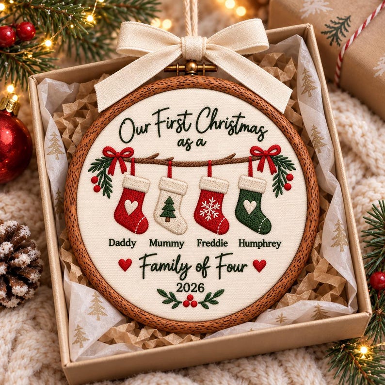 May include: A round wooden embroidery hoop ornament featuring cream fabric with embroidered text Our First Christmas as a Family of Four 2026 and four stockings labeled Daddy Mummy Freddie and Humphrey with red and green holiday accents.