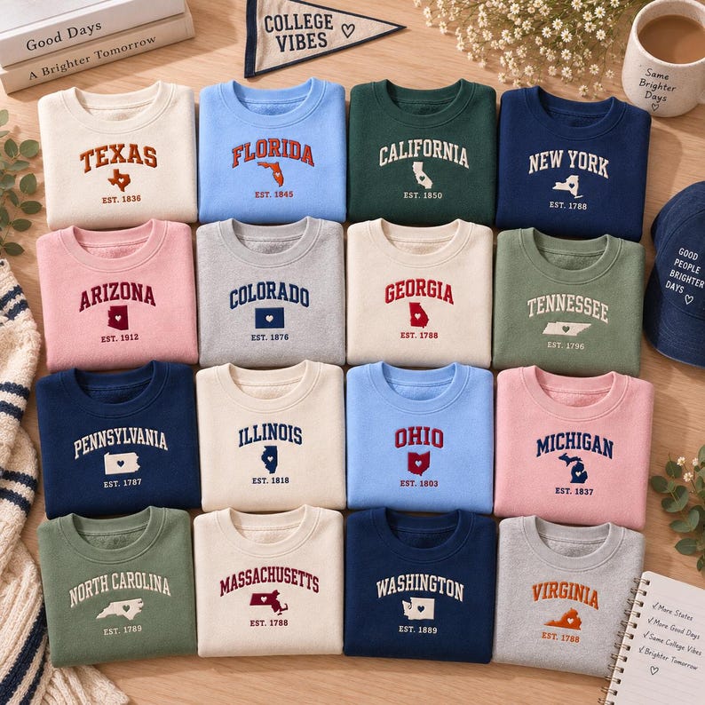 May include: A collection of sixteen crewneck sweatshirts in various colors, each featuring a state name, a map outline with a small heart, and an establishment year printed in a collegiate-style font. The sweatshirts are arranged in a grid.