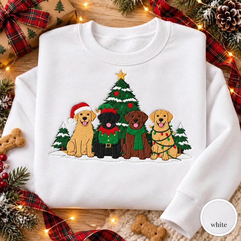 May include: A white crewneck sweatshirt featuring an embroidered graphic of four dogs sitting in front of a Christmas tree. The dogs include a yellow Labrador in a Santa hat, a black Labrador in an elf outfit, a chocolate Labrador in a green scarf, and a yellow Labrador wrapped in colorful string lights.