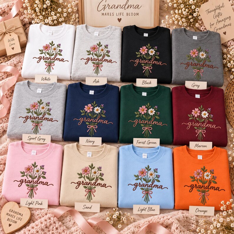 May include: A collection of twelve crewneck sweatshirts in various colors, including white, ash, black, grey, sport grey, navy, forest green, maroon, light pink, sand, light blue, and orange. Each sweatshirt features an embroidered floral bouquet with the word grandma in cursive script.