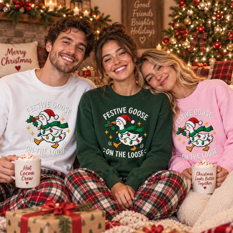 May include: Three crewneck sweatshirts in white, dark green, and light pink, each featuring a graphic of a goose wearing a Santa hat and Christmas lights with the text Festive Goose On The Loose. Two people hold mugs labeled Hot Cocoa Crew and Christmas Looks Better Together.