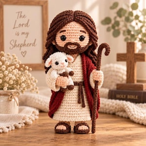 May include: A crochet doll of a figure with long brown hair and a beard, wearing a cream-colored robe with a dark red cloak and brown sandals. The figure holds a small white crochet lamb in one arm and a tall brown crochet shepherd's staff.