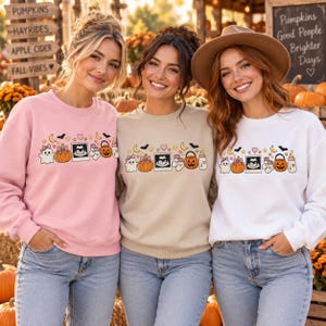 May include: Three crewneck sweatshirts in light pink, beige, and white, each featuring a graphic print of a ghost, pumpkin, ultrasound image, baby socks, jack-o'-lantern bucket, and baby bottle, accented with stars, hearts, and bats.