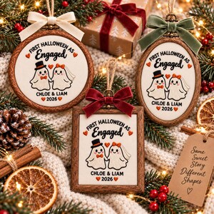 May include: Three embroidered ornaments in round, oval, and square wooden frames. Each features two ghosts, one with a top hat and one with a veil, holding hands. Text reads First Halloween as Engaged, Chloe & Liam, and 2026, with small orange hearts.