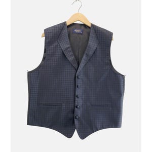 May include: A navy blue vest with a subtle checkered pattern. The vest has a notched lapel, a six-button closure, and two front pockets. It is hanging on a wooden hanger.