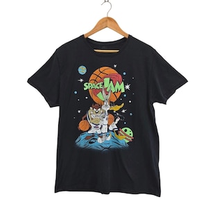 May include: Black t-shirt with a Space Jam graphic featuring Bugs Bunny, Taz, and other Looney Tunes characters. The design includes a basketball, planets, and stars. The words "Space Jam" are also visible.