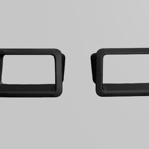 May include: Two identical matte black rectangular automotive exhaust trim bezels with rounded corners and hollow centers. These components feature a smooth, solid finish and a wide, open design intended for vehicle exterior installation.