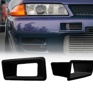 May include: Two matte black rectangular air intake ducts designed for a vehicle front bumper. These components feature a hollow center and a tapered profile, shown alongside a purple car front end with a visible headlight and front grille.