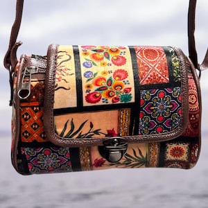 May include: A rectangular crossbody bag featuring a patchwork design of various floral and geometric patterns in vibrant colors including red, orange, yellow, and blue. The bag has a brown leather-like trim, a metal push-lock closure, and a strap.