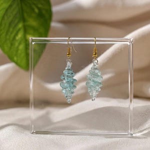 May include: A pair of drop earrings featuring light blue, spiraled glass beads shaped like elongated cones. The glass elements are suspended from gold-coloured metal fishhook wires, creating a delicate and symmetrical design for these hanging earrings.