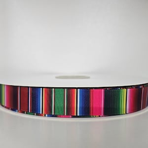 May include: A spool of colorful ribbon with a striped pattern. The ribbon features vertical stripes in various colors, including red, green, blue, and pink. The ribbon is likely made of fabric and is rolled onto a white cardboard spool.