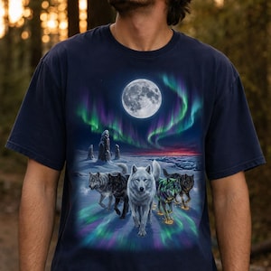 May include: A navy blue short-sleeve t-shirt featuring a graphic print of a pack of wolves walking across a snowy landscape under a full moon and vibrant green and purple aurora borealis lights in the night sky above a horizon line.