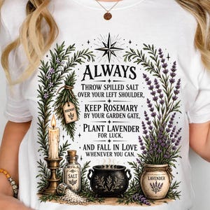 Puede incluir: Una camiseta blanca con un estampado gráfico de una vela, un frasco de sal y un caldero rodeados de ramas de romero y lavanda. El texto dice: ALWAYS THROW SPILLED SALT OVER YOUR LEFT SHOULDER, KEEP ROSEMARY BY YOUR GARDEN GATE, PLANT LAVENDER FOR LUCK, AND FALL IN LOVE WHENEVER YOU CAN.
