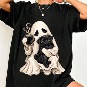 May include: A black short-sleeved t-shirt featuring a graphic print of a white ghost draped in a sheet, holding a black coffee mug with heart-shaped steam rising from it, while cradling a small black pug dog in its arms.