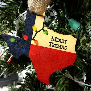 May include: A wooden ornament shaped like the state of Texas, decorated with the Texas flag and a string of colorful lights. The ornament reads "Merry Texas".