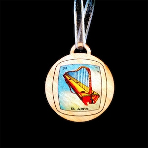 May include: A wooden ornament featuring a colorful illustration of a harp, with the text "EL ARPA" and the number "53" printed on it.