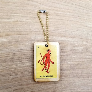 May include: A wooden keychain shaped like a playing card with a red devil figure and the text "EL DIABLITO" on a yellow background.