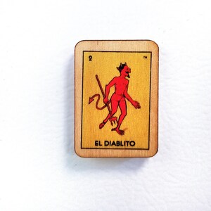 May include: A wooden playing card with a yellow background and a red devil character holding a pitchfork. The card is labeled "El Diablito" and has the number "2" in the top left corner.
