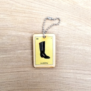May include: A wooden keychain with a black boot image and the text "LA BOTA" on a yellow background. The keychain is attached to a silver chain.