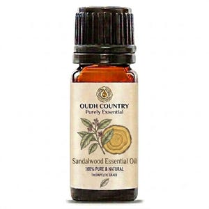 Peut inclure: Un petit flacon en verre ambré avec un bouchon noir contenant de l'huile essentielle de bois de santal. L'étiquette porte le texte OUDH COUNTRY Purely Essential, une illustration d'une branche, une coupe de bois et 100% PURE & NATURAL.