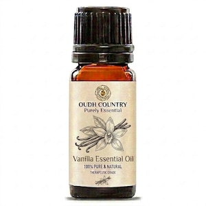 May include: A small amber glass bottle of Oudh Country Purely Essential Vanilla Essential Oil with a black ribbed cap. The label features a botanical illustration of a vanilla flower and bean, with text reading 100% PURE & NATURAL THERAPEUTIC GRADE.