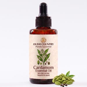 May include: An amber glass bottle with a black dropper cap containing Cardamom Essential Oil. The label features the text OUDH COUNTRY Purely Essential, Cardamom Essential Oil, and 100% PURE & NATURAL THERAPEUTIC GRADE, with a botanical illustration.