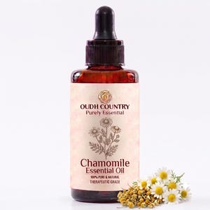 May include: A dark amber glass bottle with a black dropper cap containing Chamomile Essential Oil. The label features the text OUDH COUNTRY Purely Essential, an illustration of chamomile flowers, and the text 100% PURE & NATURAL THERAPEUTIC GRADE.