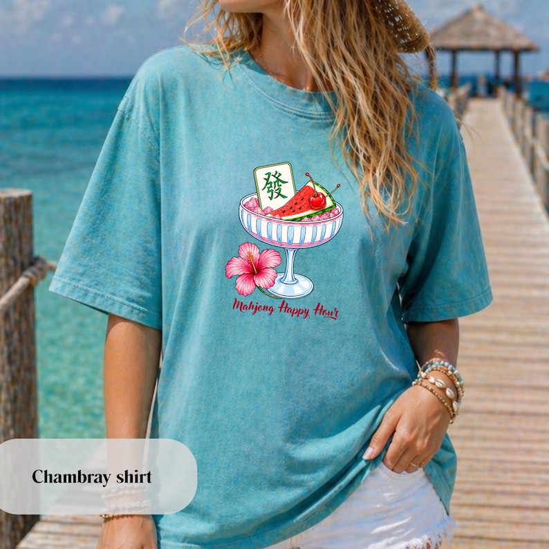 Peut inclure: Un t-shirt bleu sarcelle &agrave; manches courtes orn&eacute; d'un motif repr&eacute;sentant un bol en verre rempli de tranches de past&egrave;que, d'une cerise et d'une tuile de mah-jong avec le caract&egrave;re Fa. Une fleur d'hibiscus rose et le texte Mahjong Happy Hour.