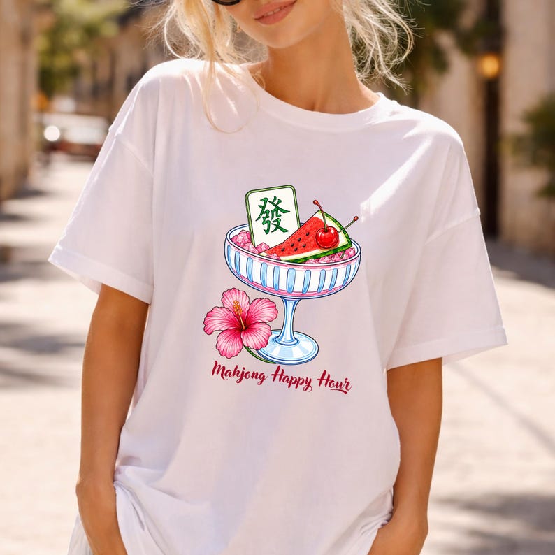 Peut inclure: Un t-shirt blanc avec un motif repr&eacute;sentant un bol en verre &agrave; bord bleu rempli de glace rose, une tranche de past&egrave;que, une cerise rouge et une tuile de mah-jong verte avec le caract&egrave;re "發". Une fleur d'hibiscus rose et le texte "Mahjong Happy Hour".