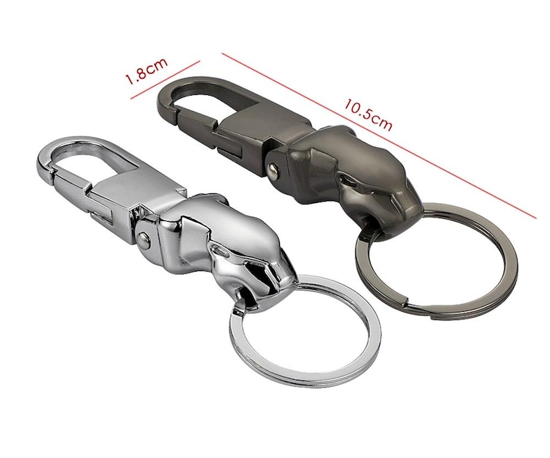 May include: Two metal keychains featuring a jaguar head design, one in a polished silver finish and one in a dark gunmetal gray finish. Each keychain includes a spring-loaded clasp and a circular ring, with dimensions of 1.8 cm width and 10.5 cm length.