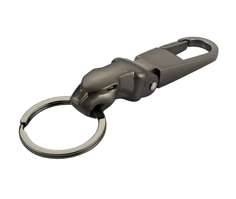 May include: A gunmetal-colored keychain featuring a stylized jaguar head sculpture. The jaguar head is attached to a metal spring-loaded carabiner clip on one side and a circular split ring for keys on the other side, with a smooth metallic finish.