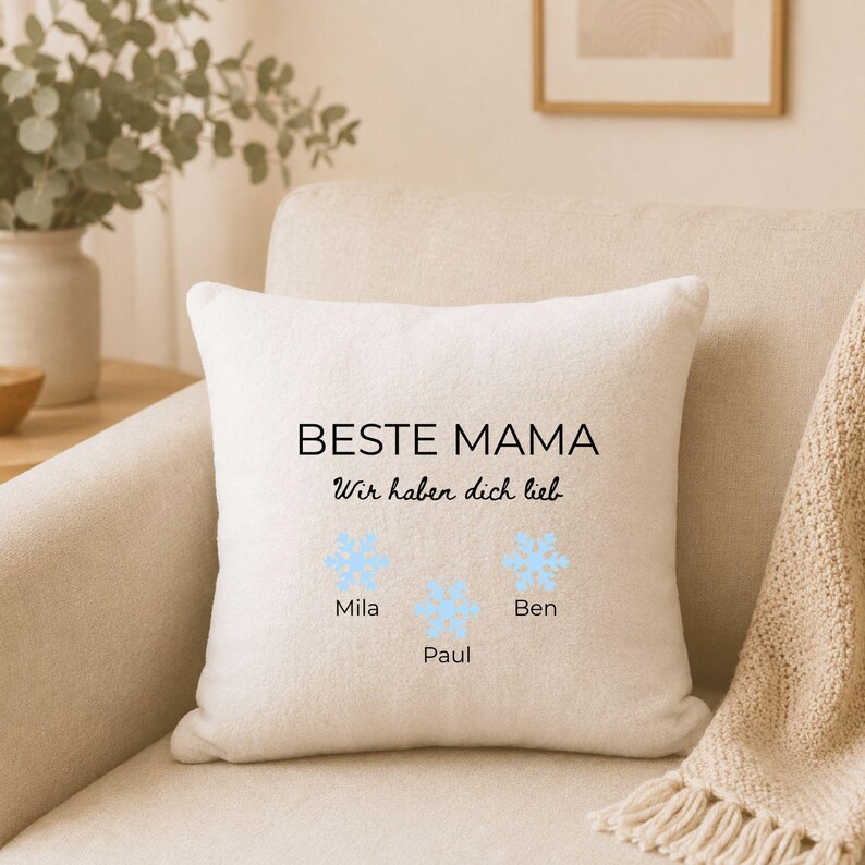 May include: A square off-white throw pillow featuring the black text BESTE MAMA and Wir haben dich lieb. Below the text are three light blue snowflake illustrations with the names Mila, Paul, and Ben printed in black underneath each snowflake.