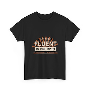 Può includere: Una t-shirt nera a maniche corte con un design grafico che riporta il testo "CERTIFIED FLUENT IN PROMPTS" in bianco e arancione, con un elemento a raggiera sopra il testo e "ONE MORE ITERATION - NO HALLUCINATIONS" stampato sotto.
