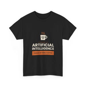 Può includere: Una t-shirt nera a maniche corte con la grafica di una tazza da caffè con un volto da robot. Sotto la tazza, il testo recita POWERED BY ARTIFICIAL INTELLIGENCE, seguito da un blocco rettangolare arancione con il testo FUELED BY REAL COFFEE.