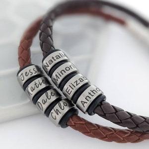 May include: Two braided leather bracelets in dark brown and medium brown tones. Each bracelet features multiple cylindrical silver-toned metal beads engraved with the names Jessie, Katie, Dale, Chloe, Natalie, Minori, Elizabeth, and Anthony.
